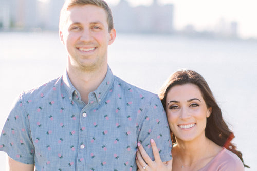 Couple smiling in a lakeside engagement photo with Glamour Girl makeup