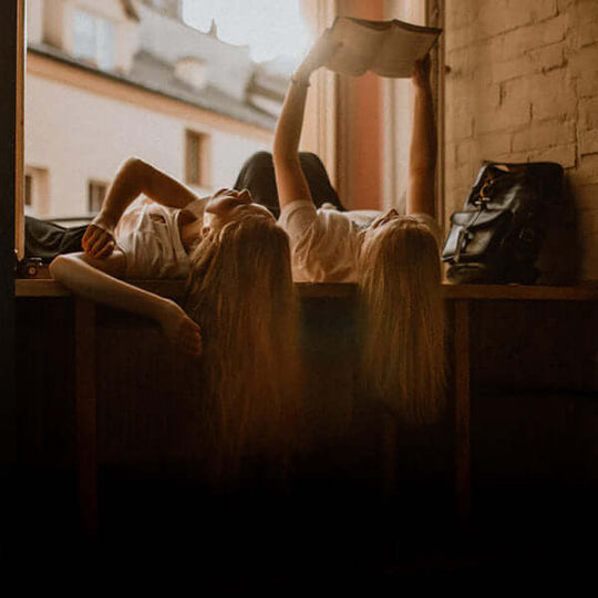 Two women enjoying a book while basking in the warm glow of a stunning sunset, a peaceful and relaxing scen