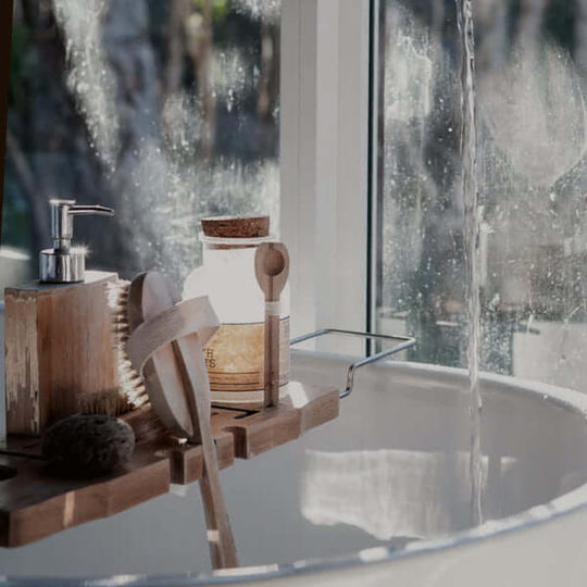 Image of a white bathtub with a variety of skincare products including a loofah, soap, and other personal care items. The tub is clean and minimalist in design.